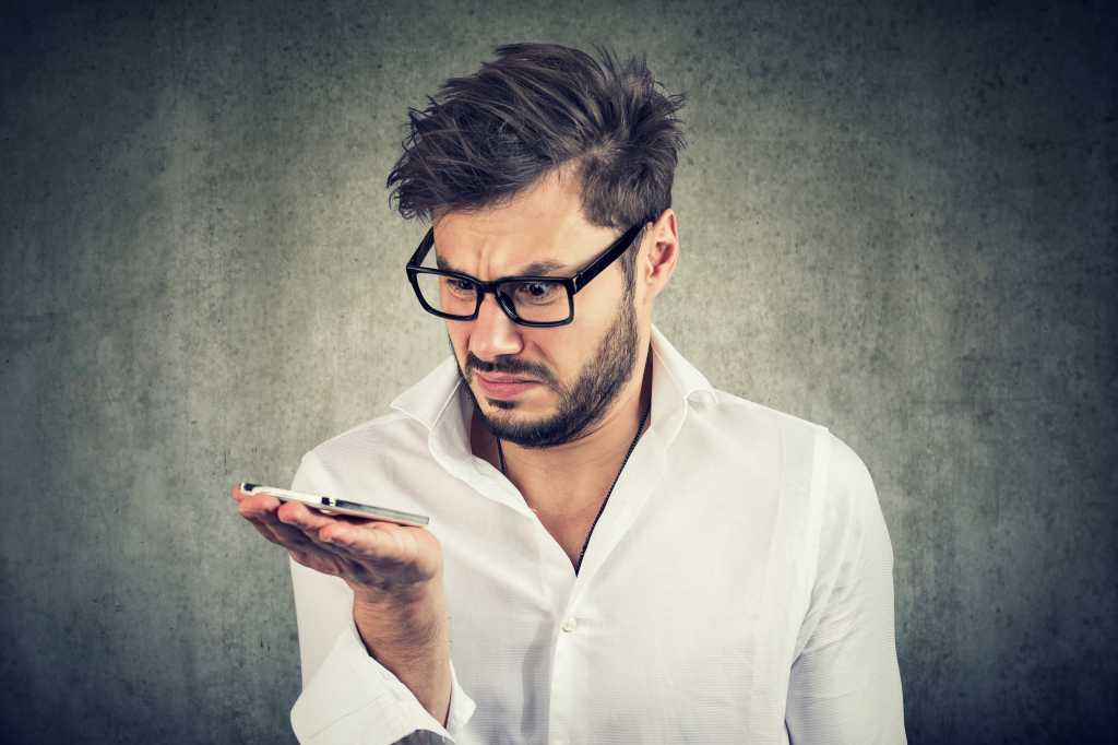 Bearded man glares at mobile phone in his hand.