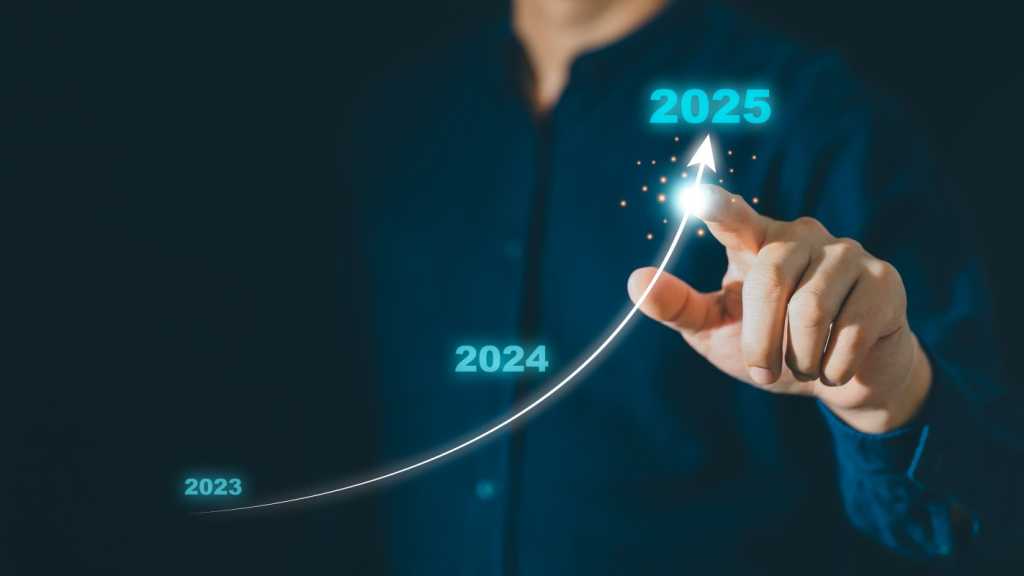 A man holding out his index finger pointing at an arrow curving upward. Along the line of the arrow are the numbers 2023, 2024 and 2025.