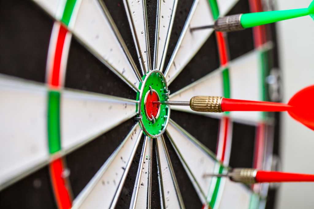 close up of dartboard and red and green darts with bullseye hits and misses