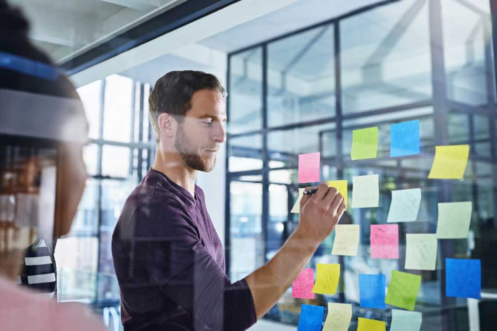 Business people, planning and writing on sticky note for ideas, solution and scrum or agile of creative project. Public relations leader with training, presentation or teamwork for workflow on glass