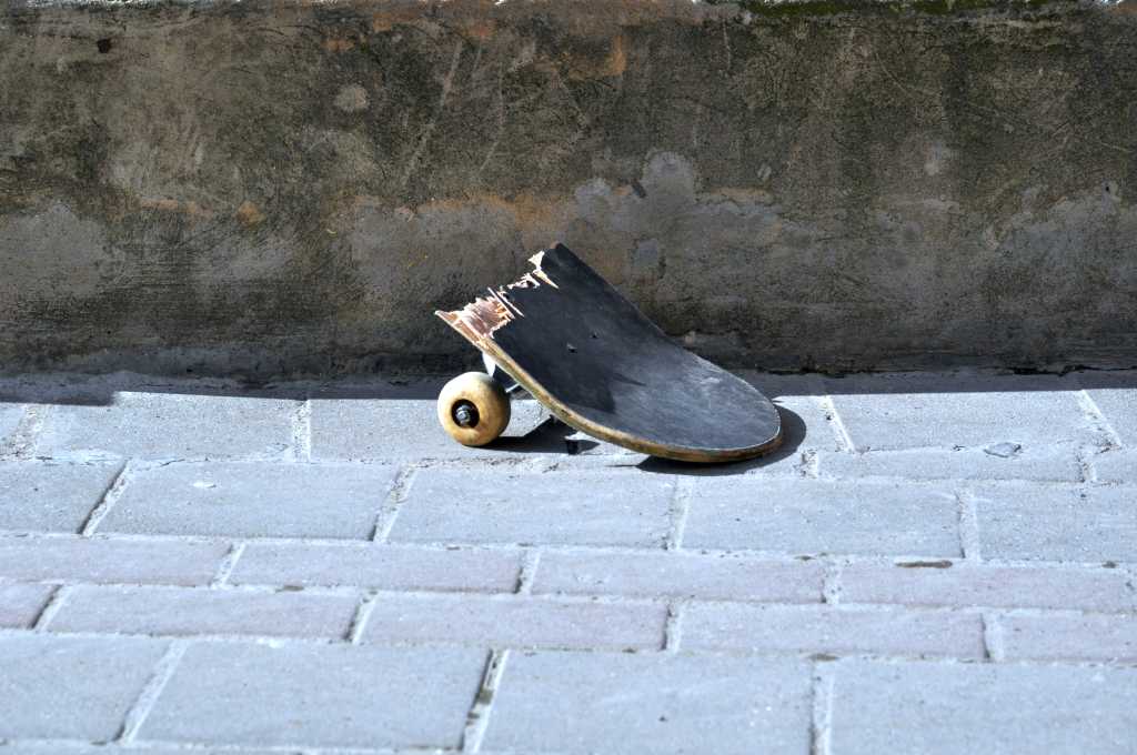 Half a broken skateboard rests on a gray cobblestone path.